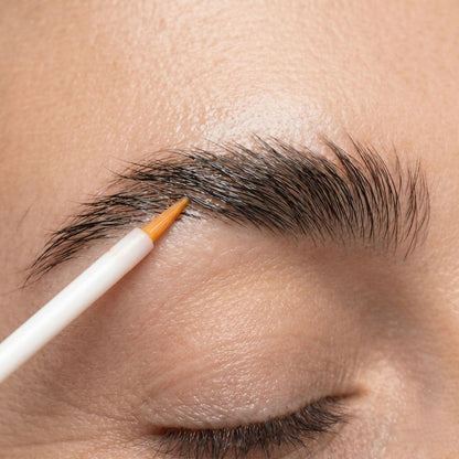 Eyebrow growth serum with a small brush on a close-up of skin